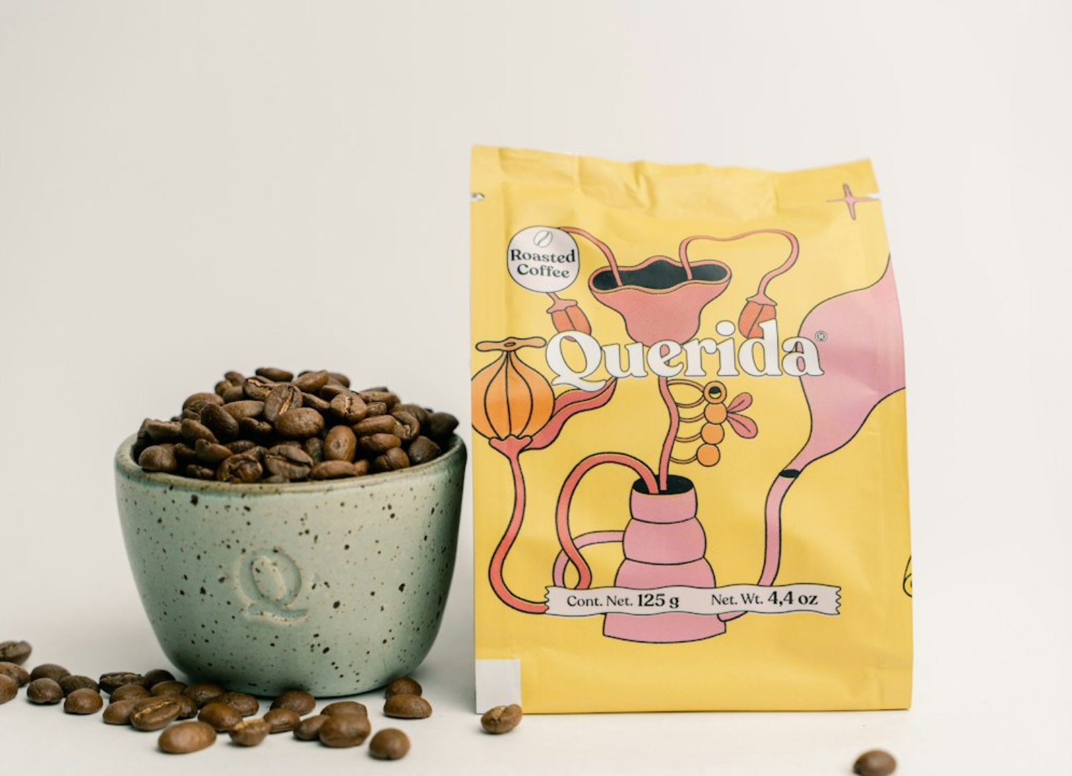 A yellow bag of roasted coffee beside a speckled ceramic cup full of beans